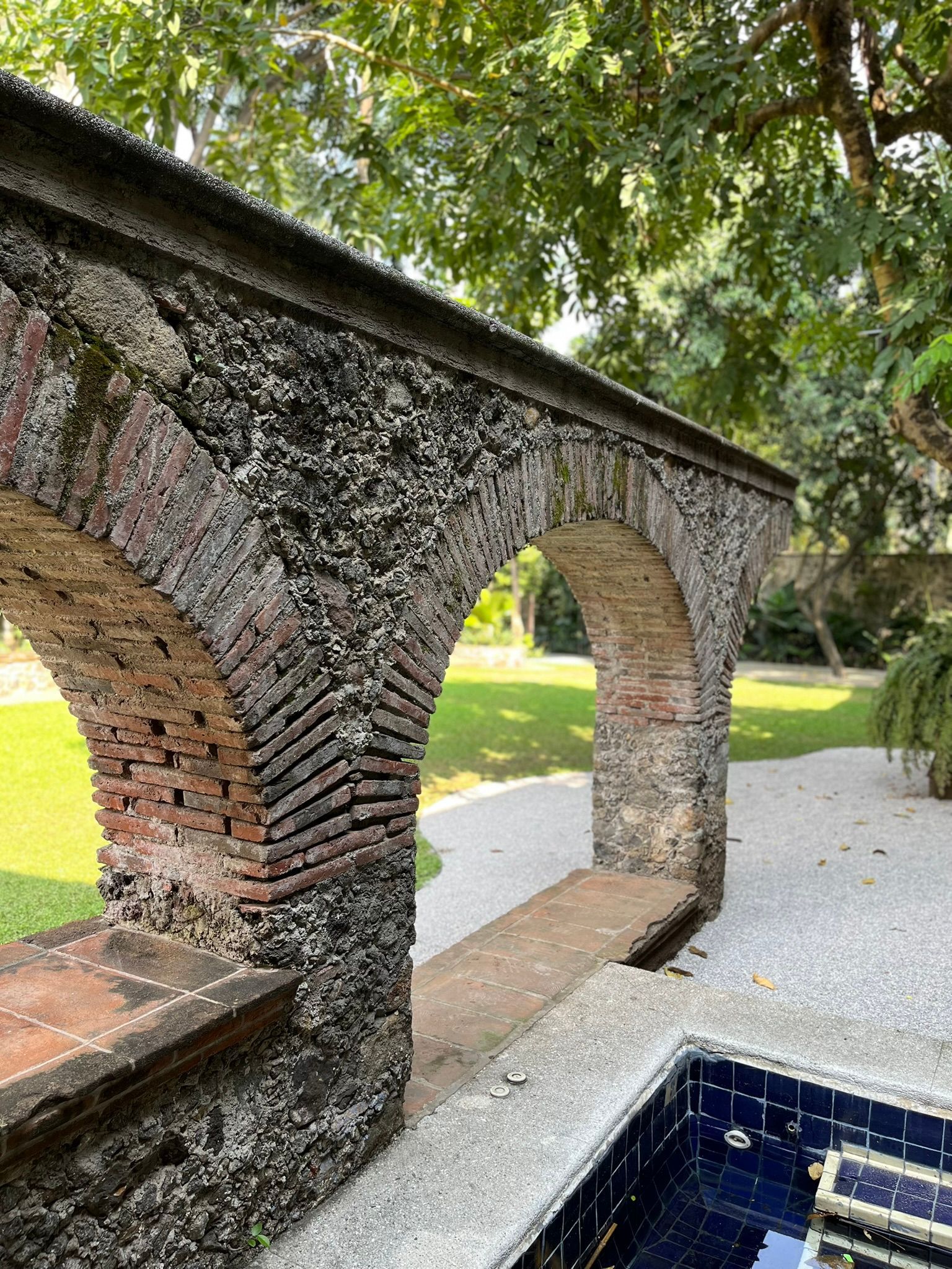 Arco de ladrillo y piedra con vistas a un jardín con piscina.