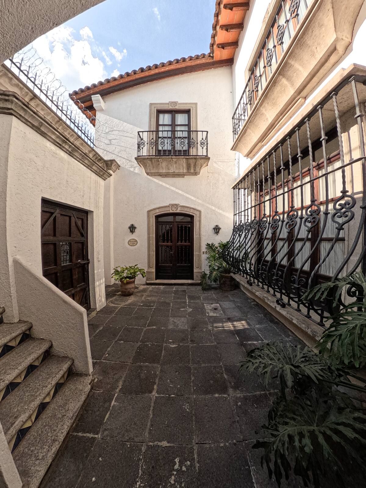 Patio con edificios blancos, puertas de madera oscura, rejas de hierro y pavimento de piedra.