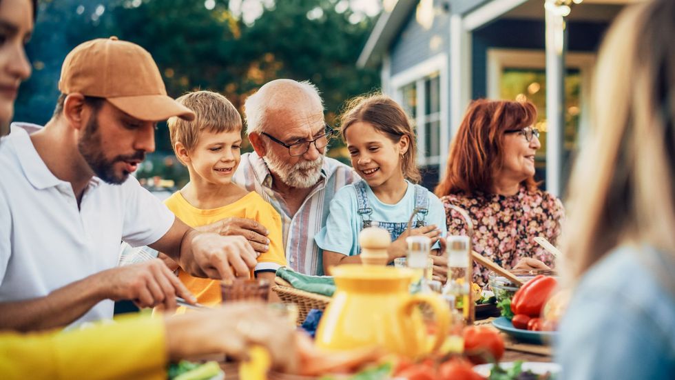 Family gathered around an outdoor table sharing food and conversation at a sunny picnic