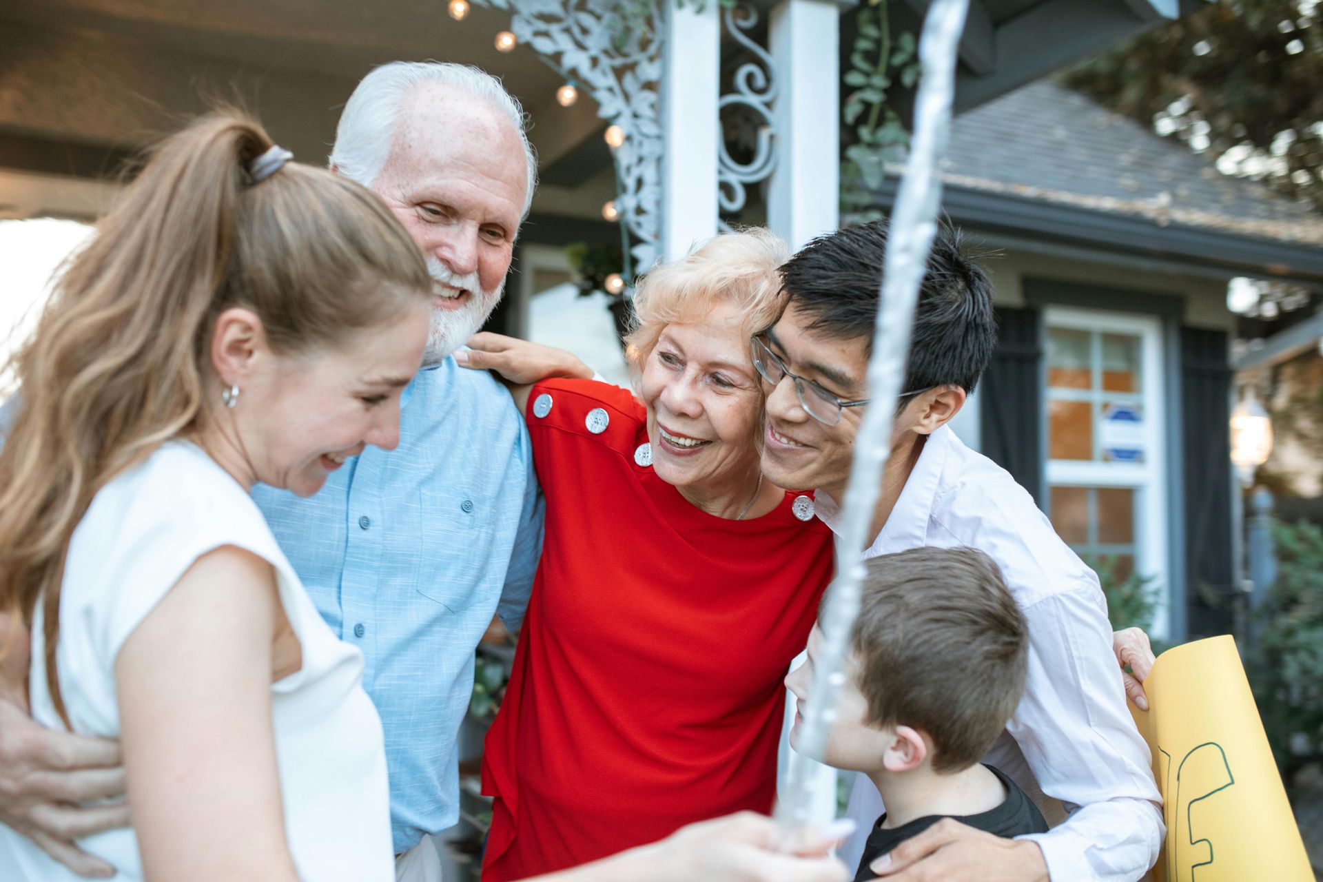 Family group hugging outside a house, smiling and holding a young child