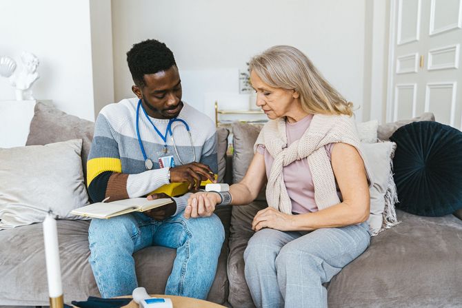 Two people sit on a couch, discussing a book and a small object in a bright living room.