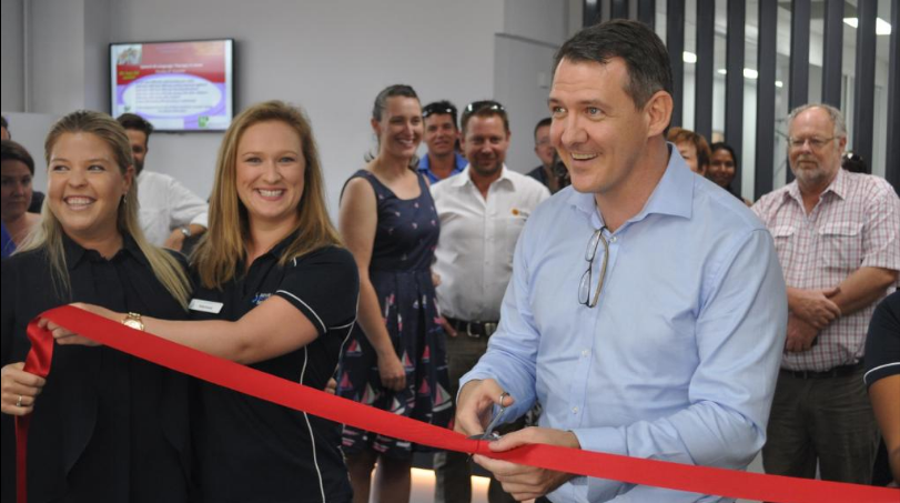 A man is cutting a red ribbon in front of a group of people.
