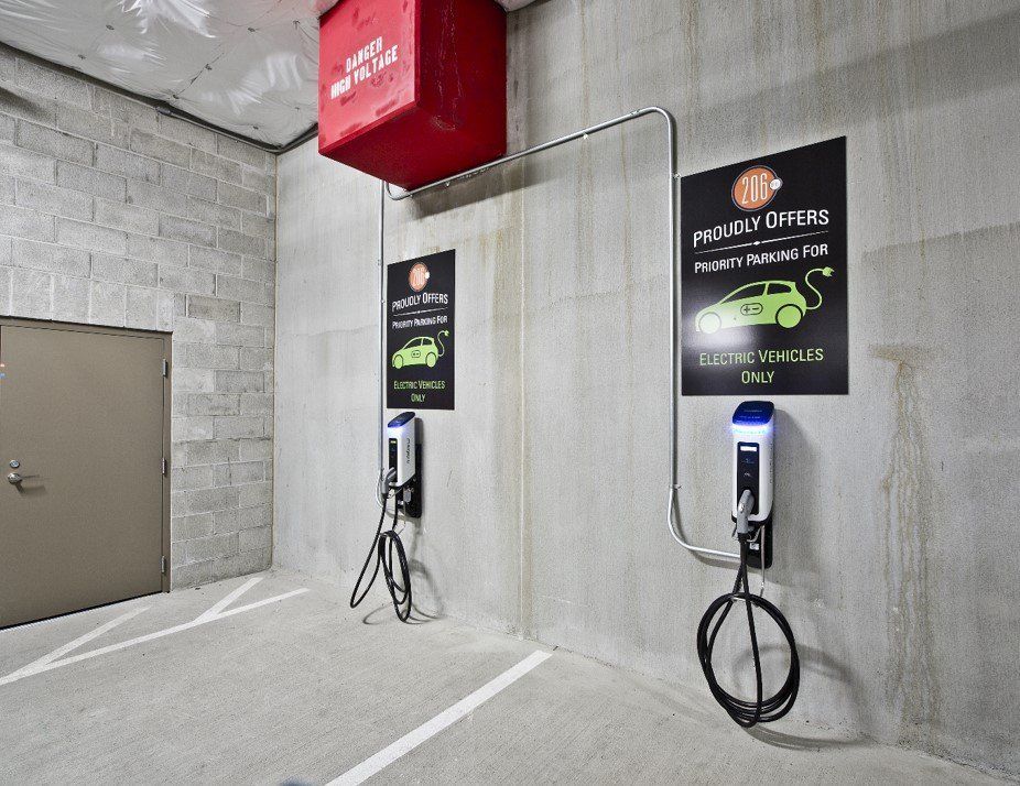 Two electric vehicle charging stations mounted on a concrete wall in a parking garage with signage above each unit.