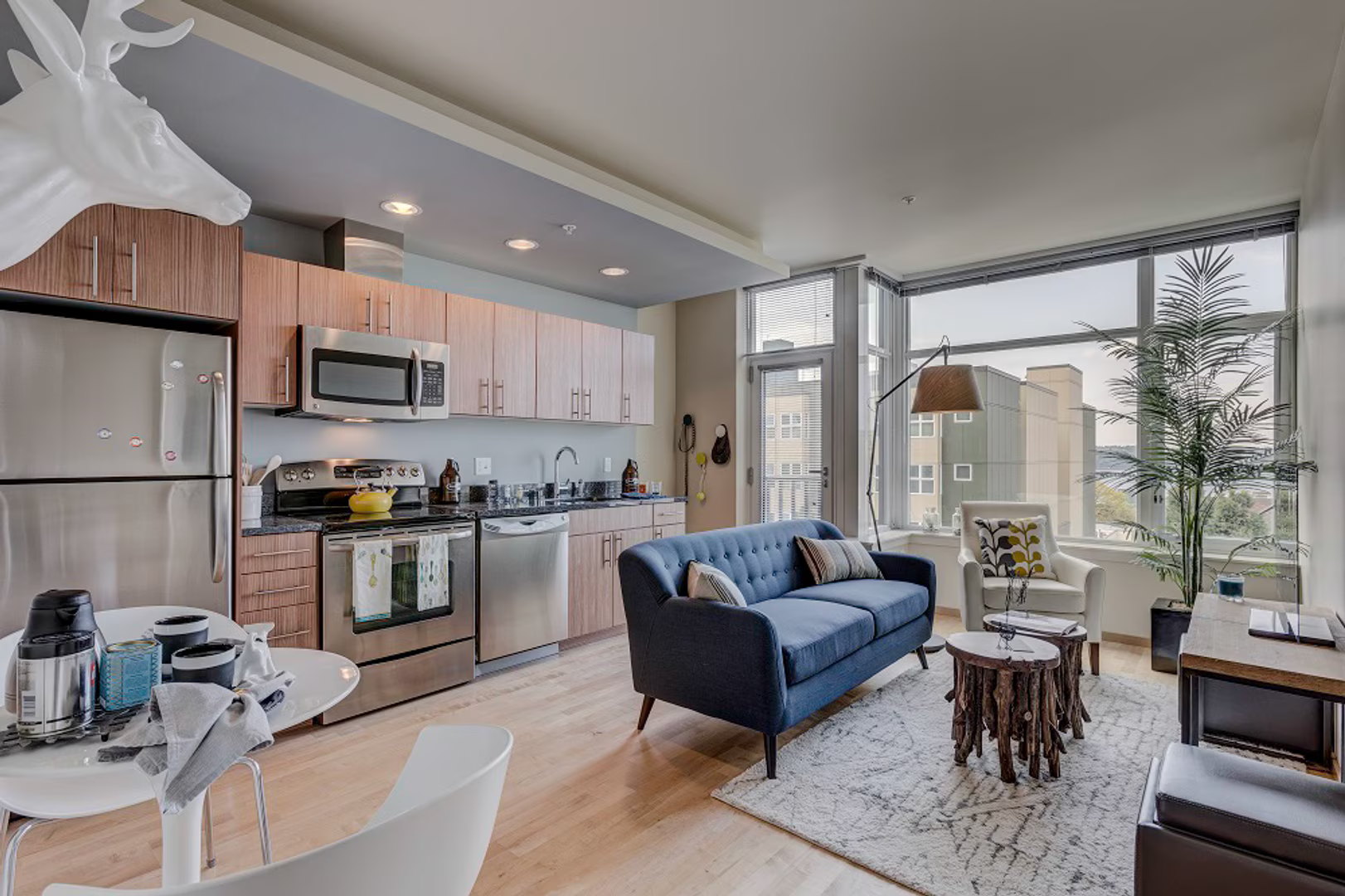 A modern, open-plan apartment with a kitchen, dining area, and a blue sofa in a brightly lit living space.