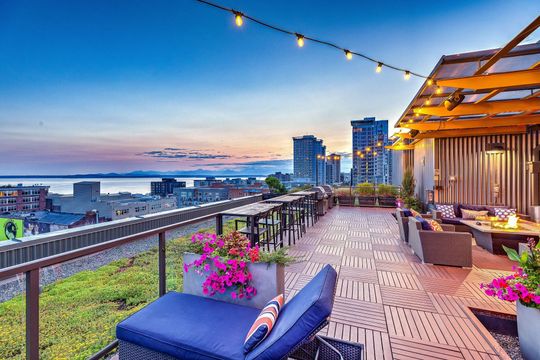 Rooftop terrace with string lights, lounge seating, and a city skyline view.