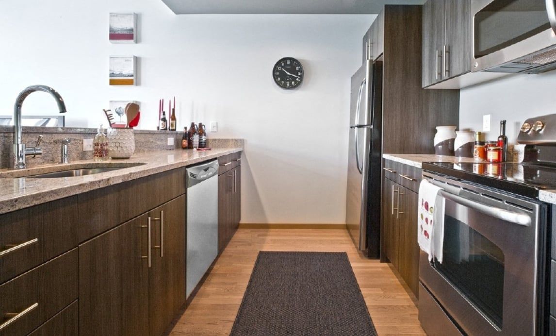 Modern apartment kitchen with dark wood cabinets, stainless steel appliances, and a runner rug.
