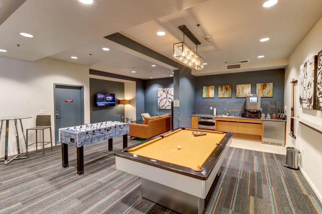 Indoor community recreation room with pool table, foosball, seating area and kitchenette.