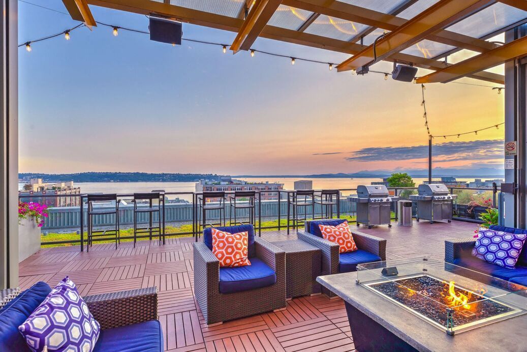 Rooftop lounge with cushioned seating, a fire pit, and grilling stations overlooking the water.