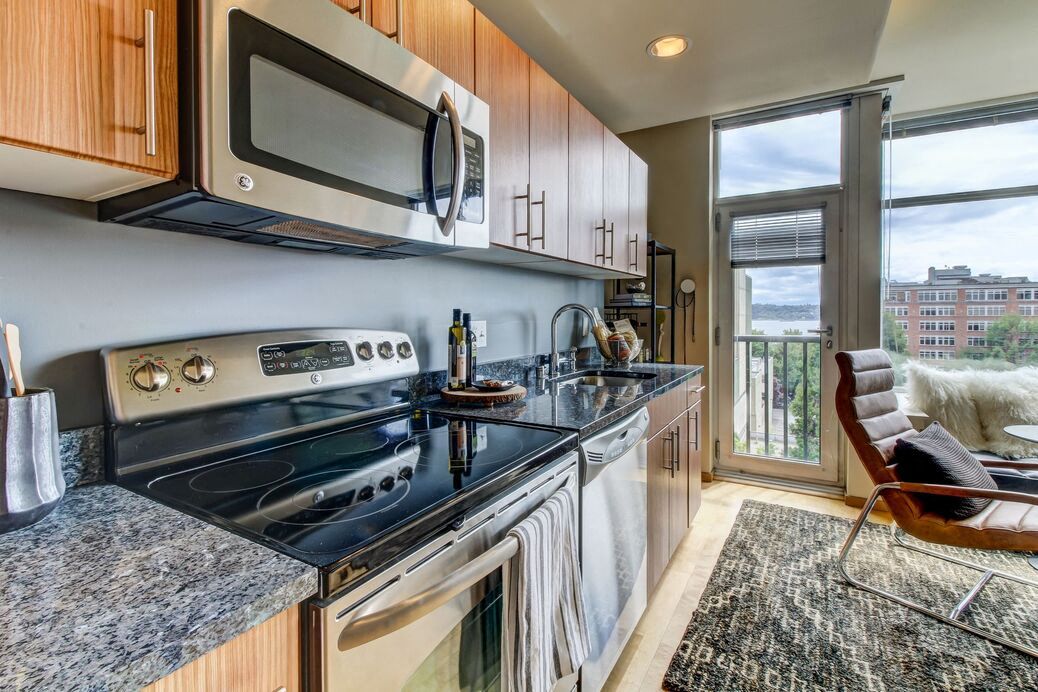 Modern apartment kitchen with stainless steel appliances and a balcony with city view.