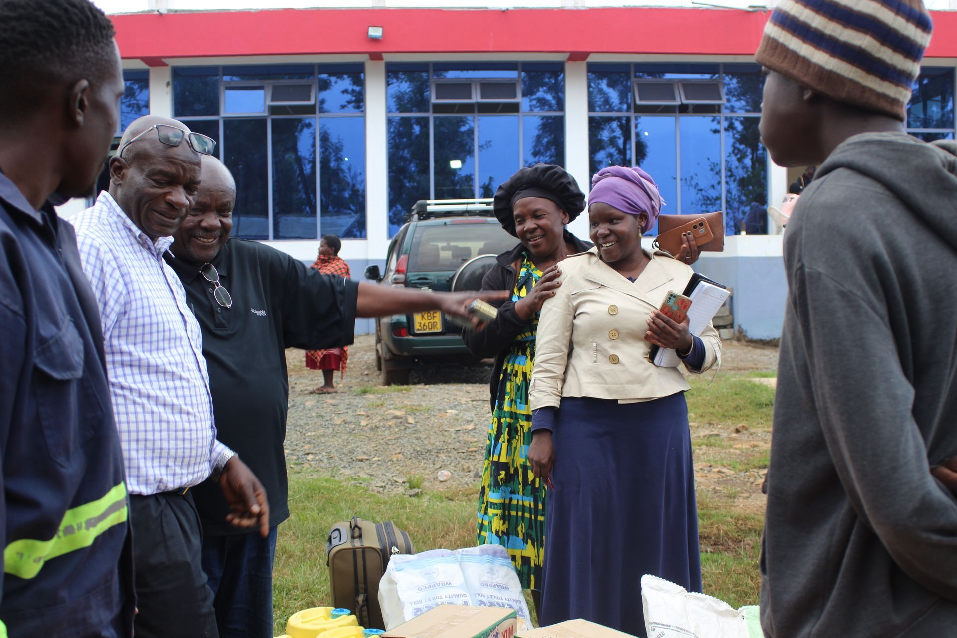 Group of people outdoors in front of a building; some pointing and talking around supplies.