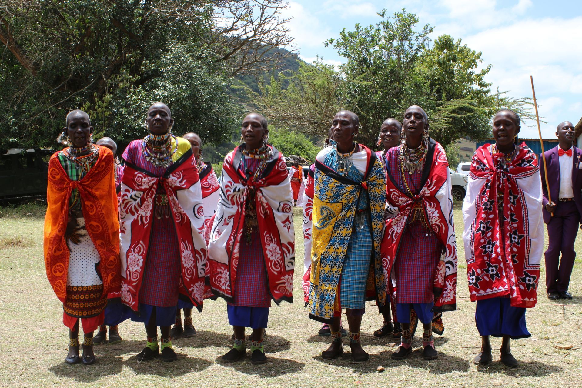 Group of people in colorful patterned cloaks and jewelry standing outdoors.