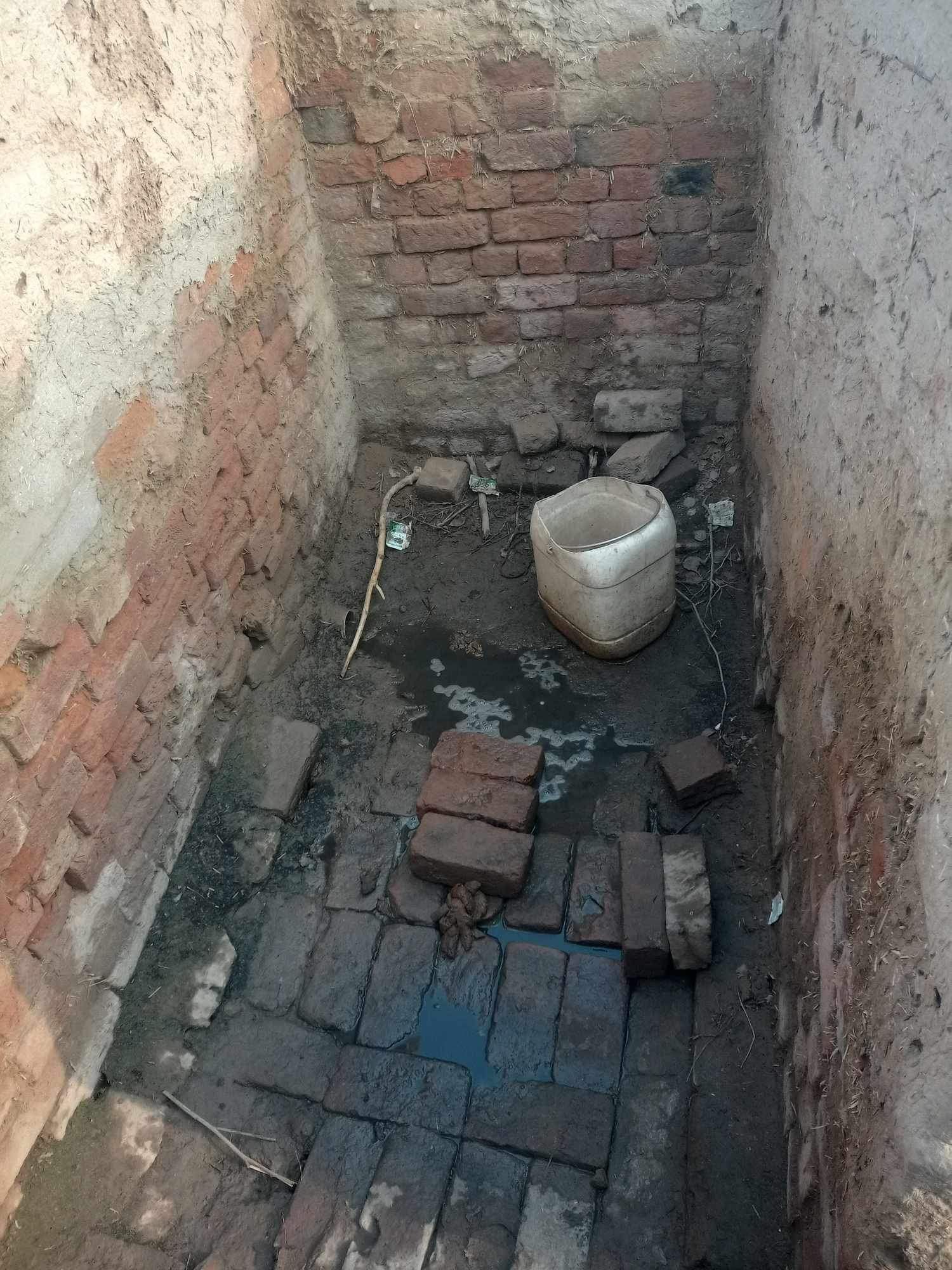 Brick-lined, small, damp room with a bucket and scattered bricks on the floor.