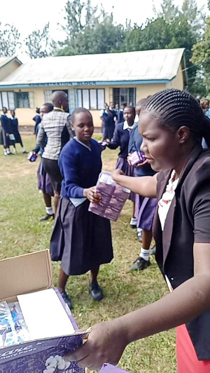Teacher distributing items from a box to students wearing uniforms in front of a building.