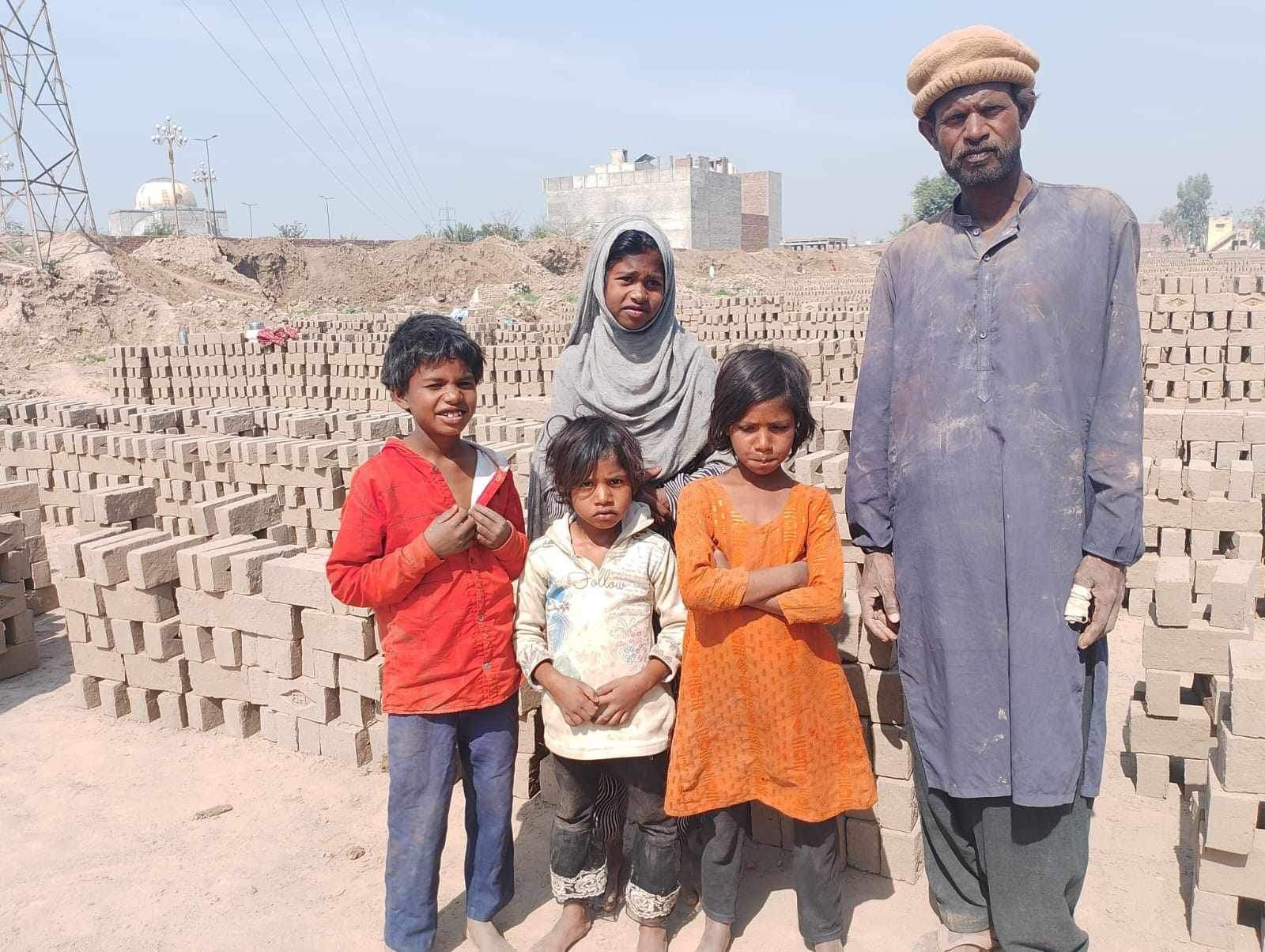 Family posing in front of brick stacks, in a dusty outdoor setting.