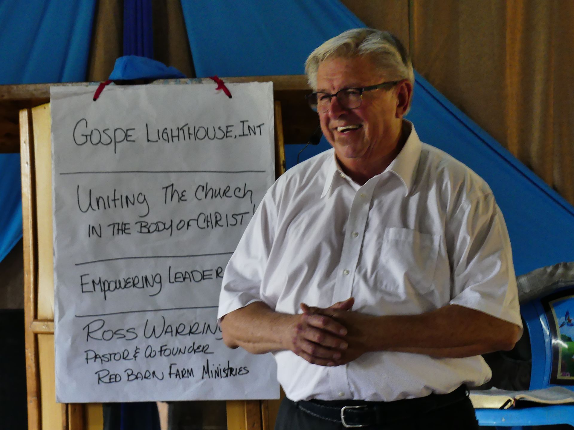 Man speaking in front of a sign:
