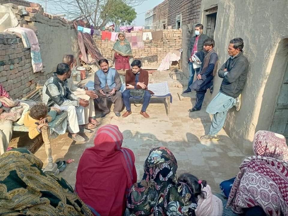 Group of people gathered outdoors, some seated, some standing, in a courtyard. People are facing each other.