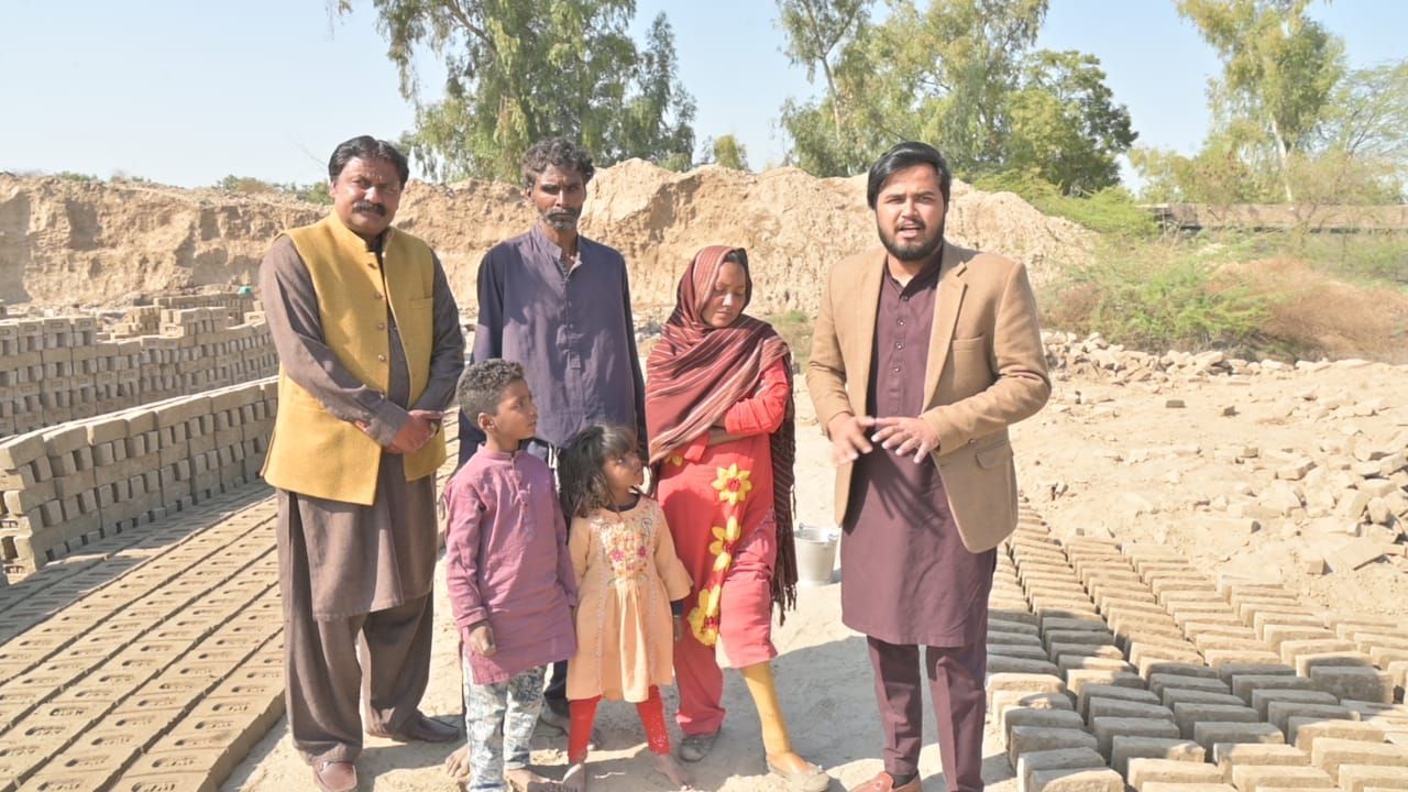 Group of people standing near brick stacks outdoors. One person holding a shovel.