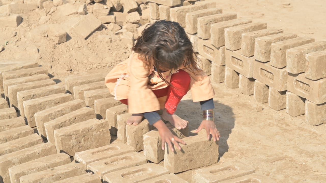 Child arranging bricks in a dusty outdoor setting.