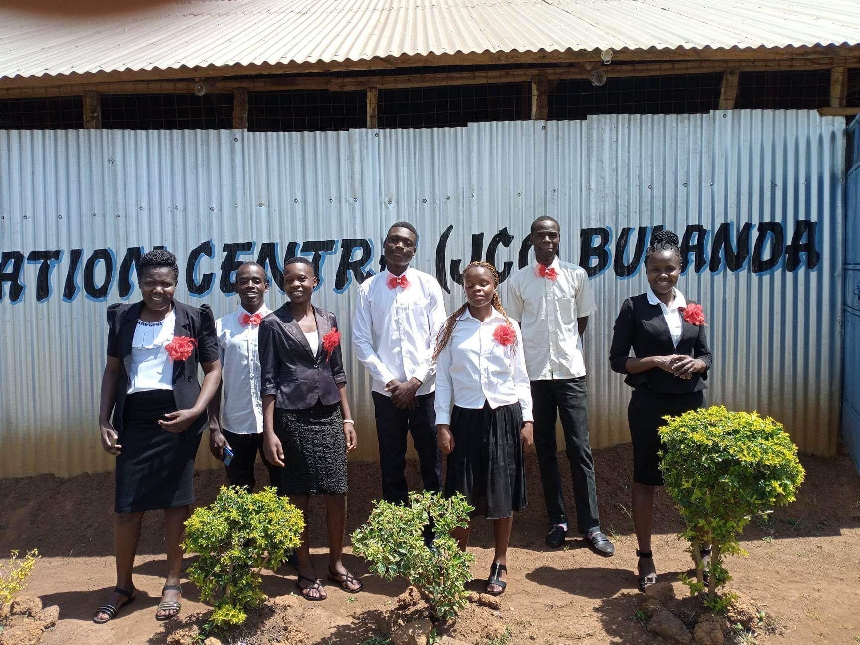 Group of people in business attire in front of a building. They are wearing red corsages.