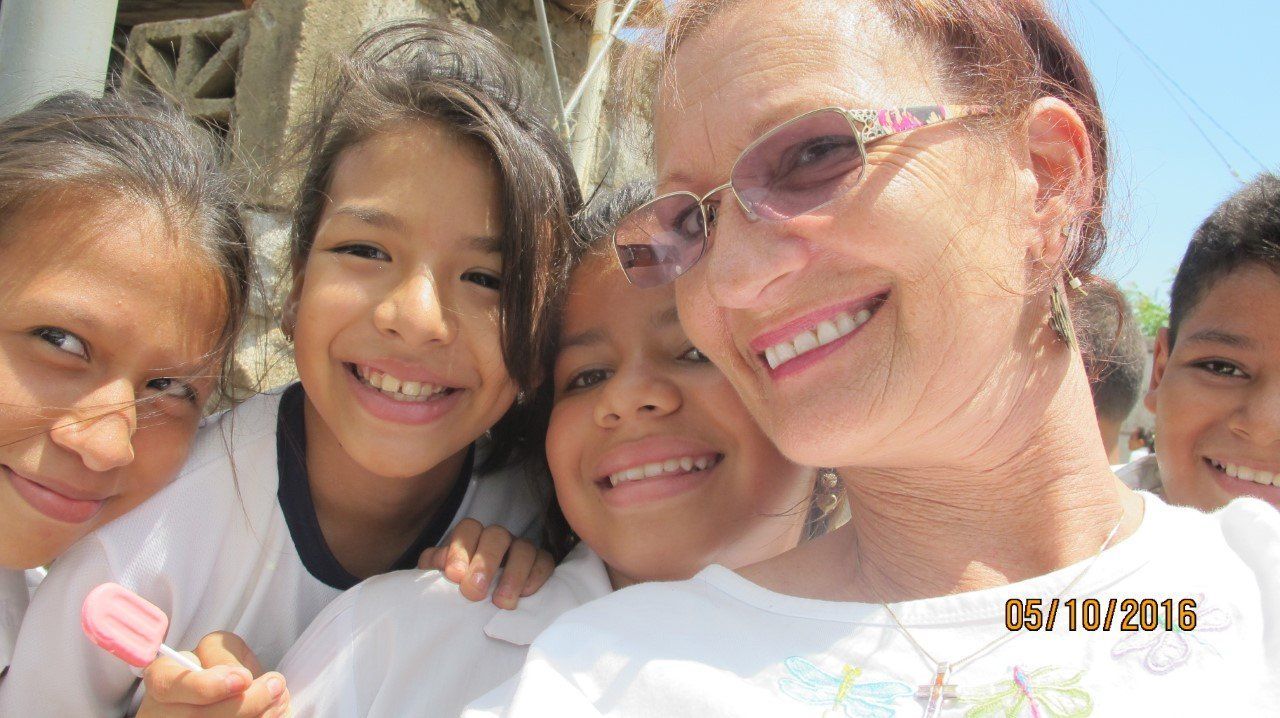 Woman smiles with several children outdoors.