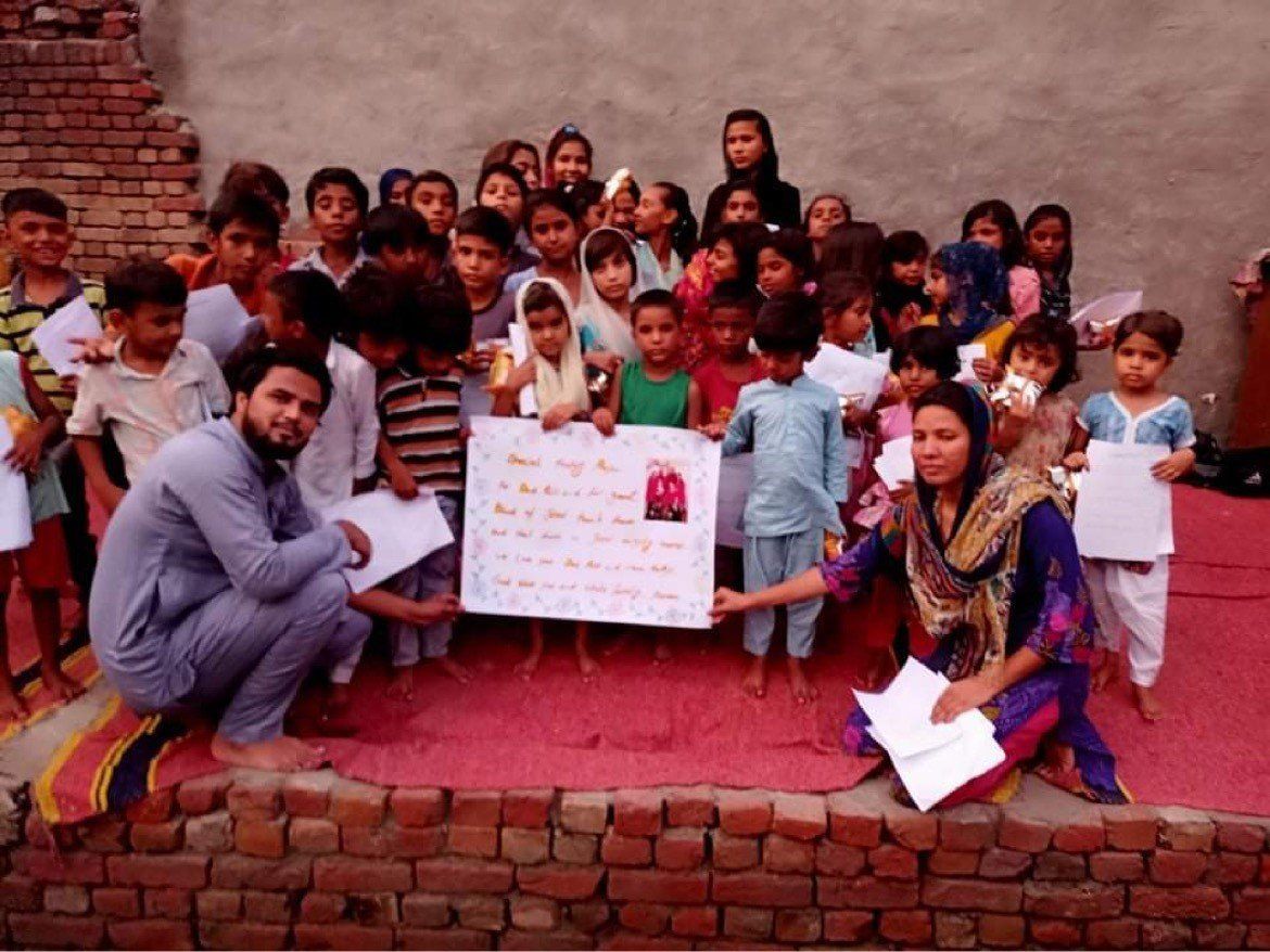 A group of children and two adults holding a sign and papers, standing on a red surface.