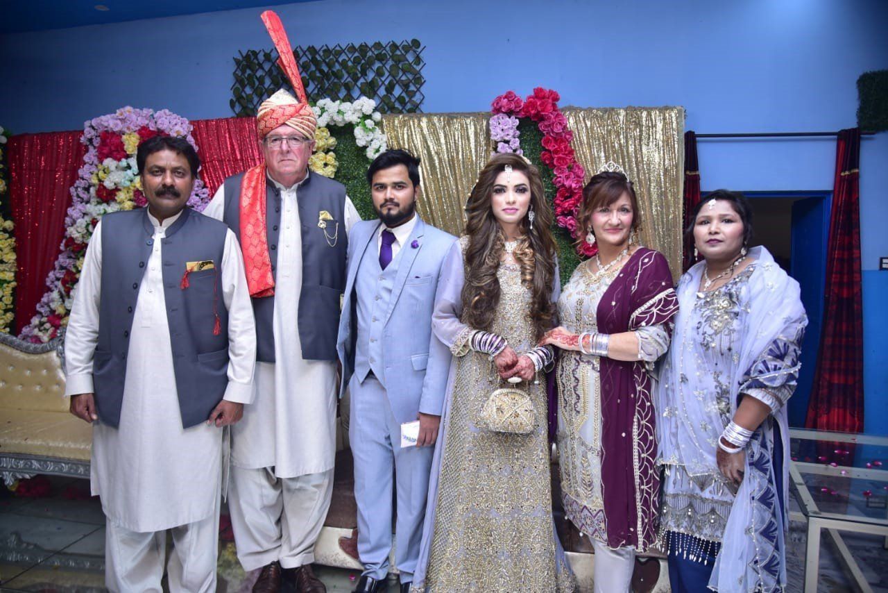Group of six people posing for a photo at a decorated event with a bride wearing a beaded gown.
