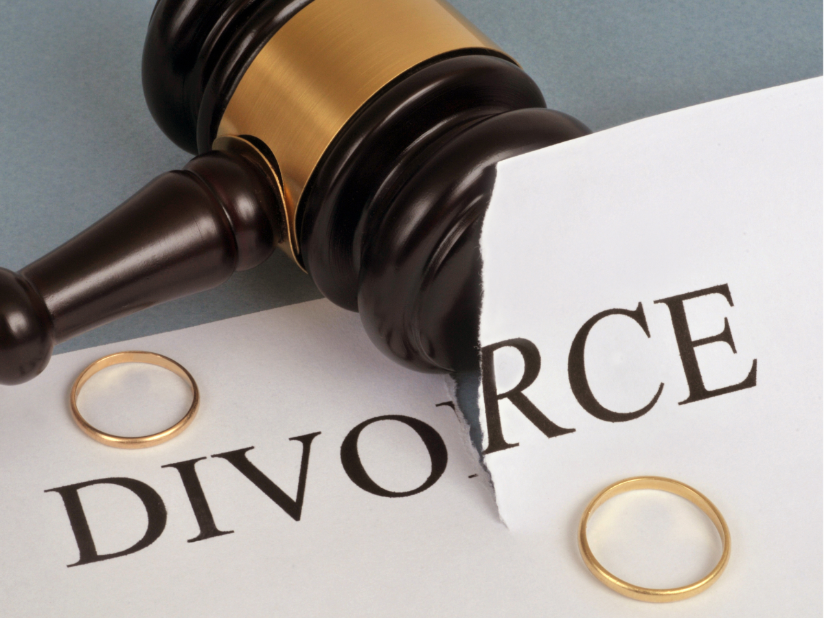 Gavel over a torn divorce document with wedding rings on a gray surface