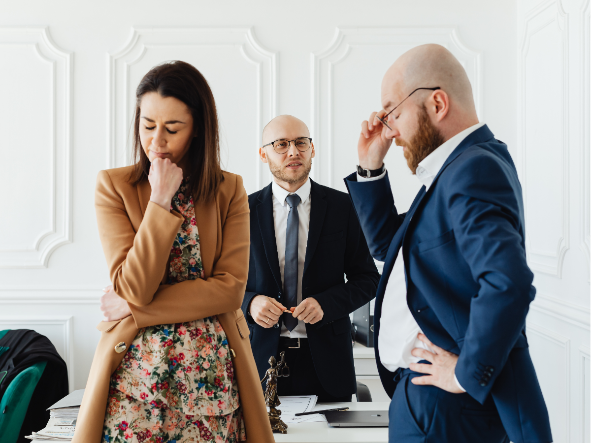 Three office workers in a meeting, looking stressed and thoughtful in a bright conference room