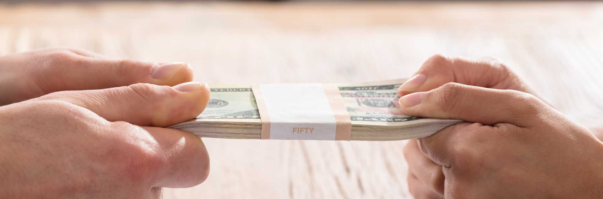 Two hands exchanging a stack of cash across a table