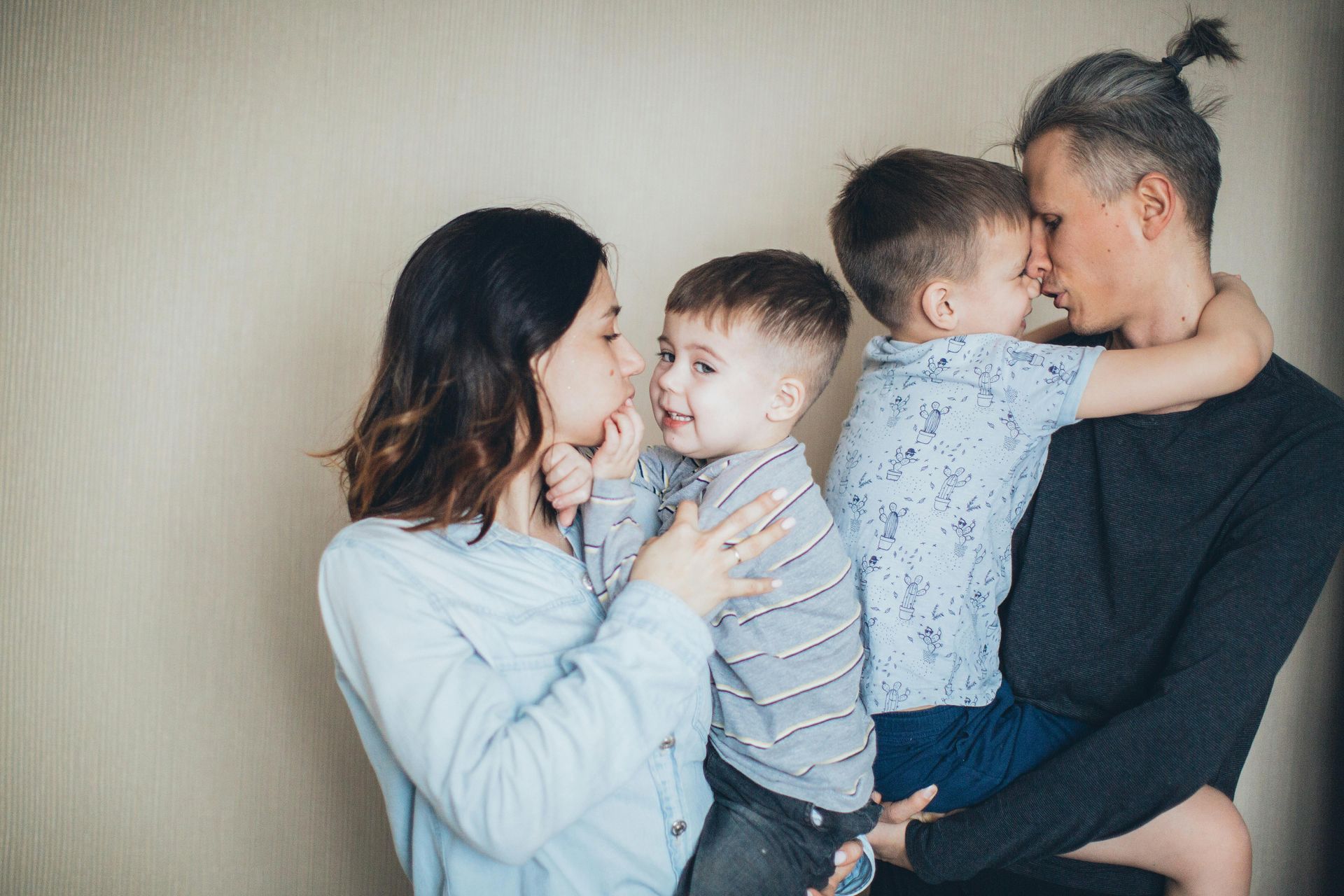 Two adults holding two children in a warm family hug against a plain beige wall