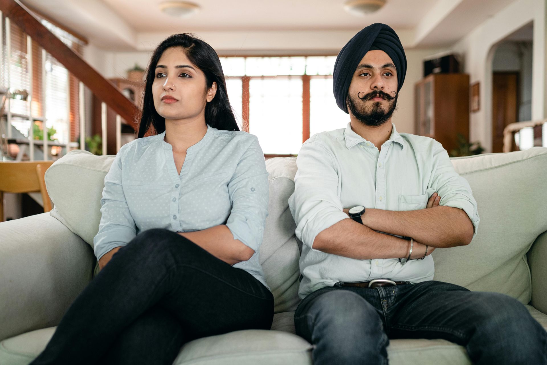 Two people sitting on a couch with arms crossed in a bright living room