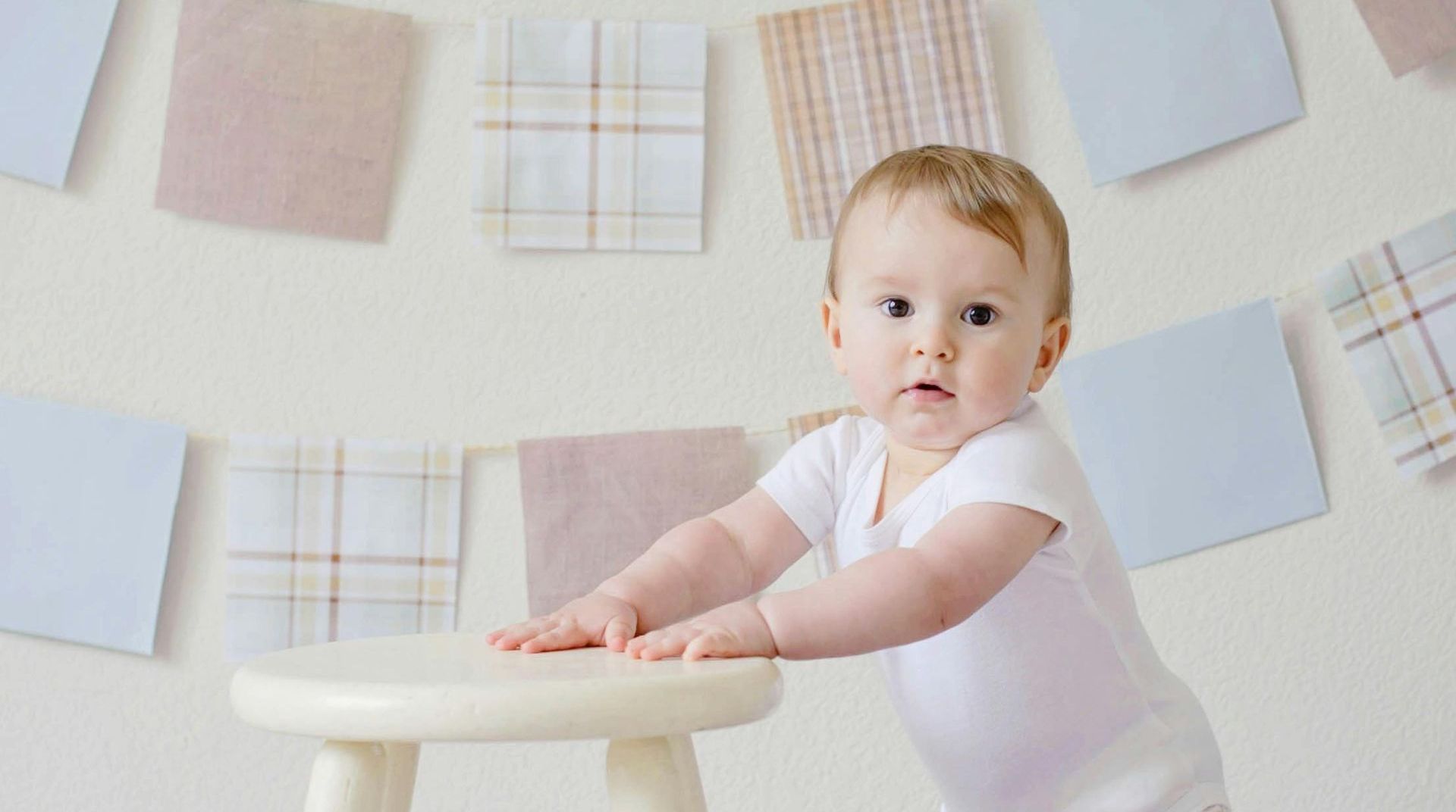 A baby is standing on a small white stool.