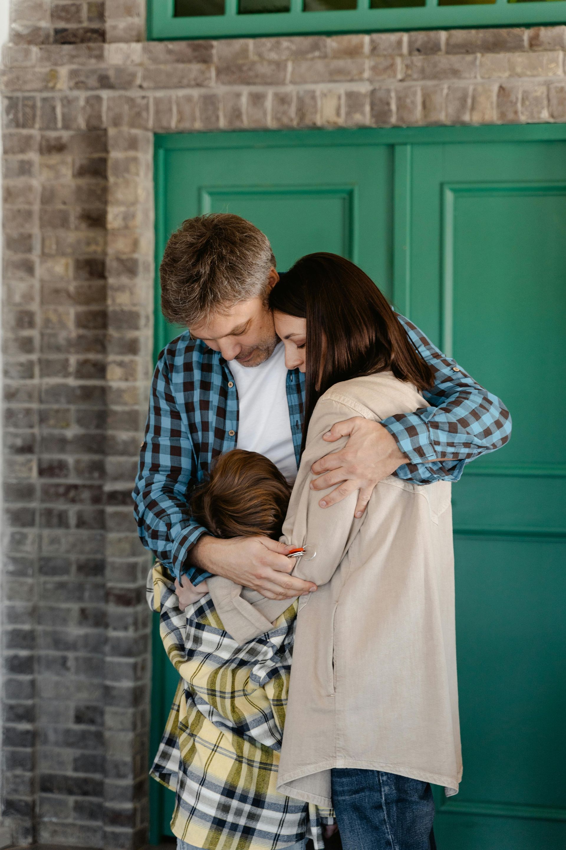 Family hugging in front of a teal door, with one child wearing a plaid shirt and jacket