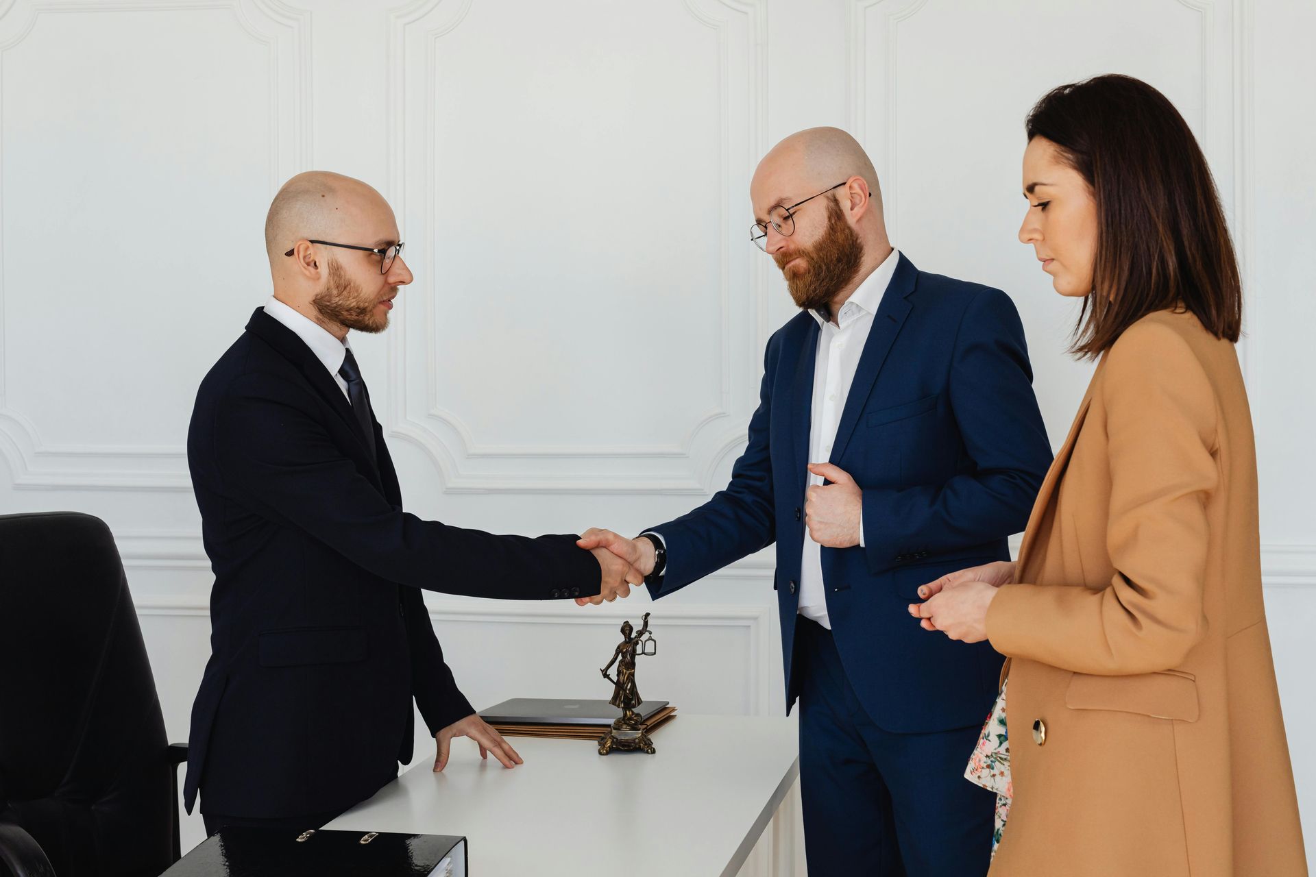 Two professionals shaking hands in an office, with a woman standing beside them.