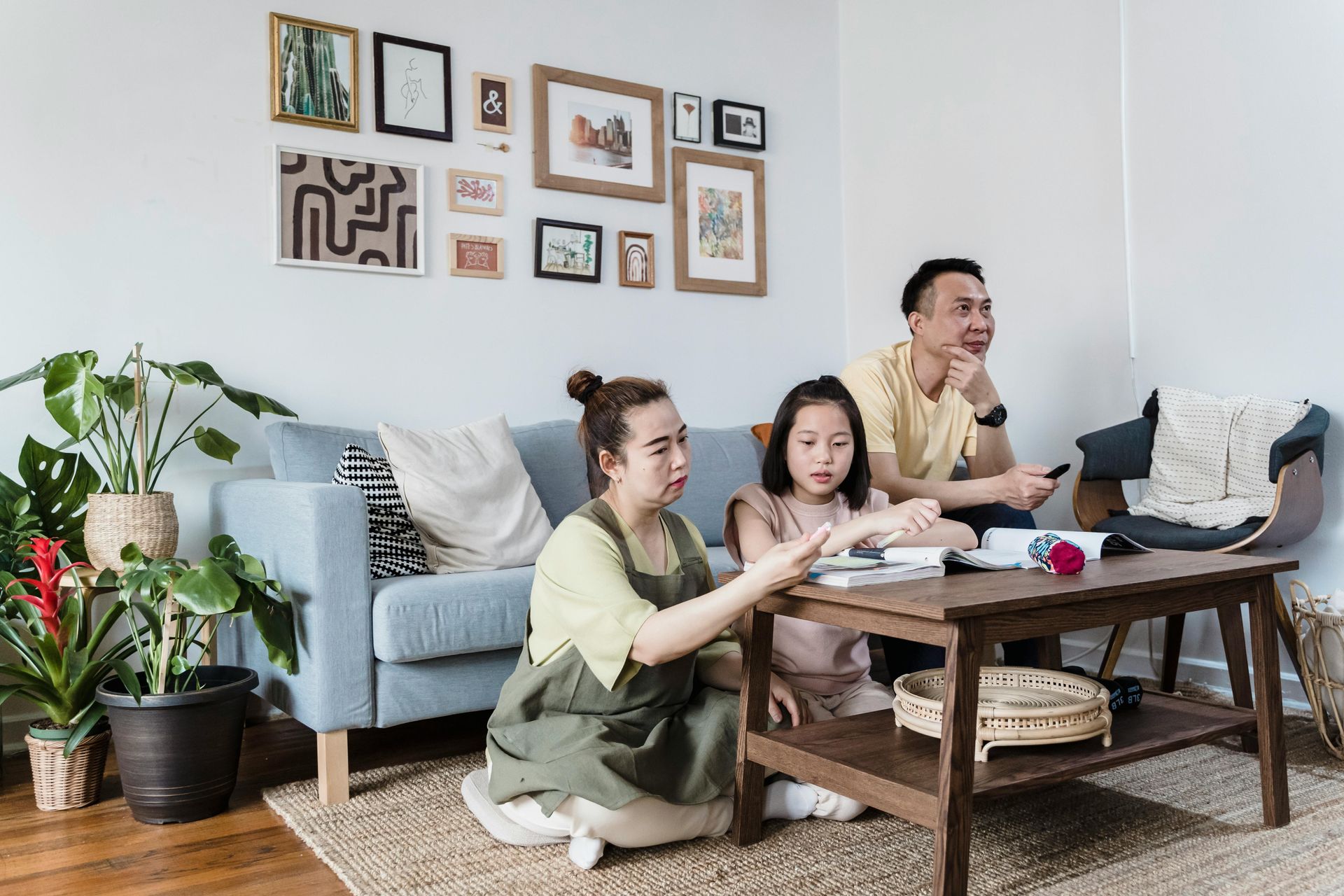 Three people on the floor at a coffee table in a bright living room, working and eating together