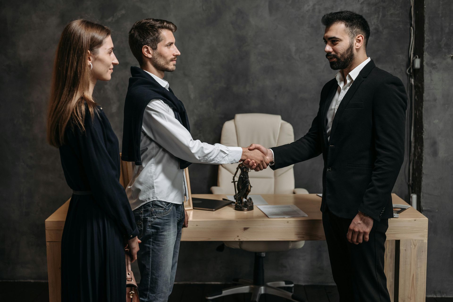 Three coworkers in business attire shake hands across a conference table in a modern office.