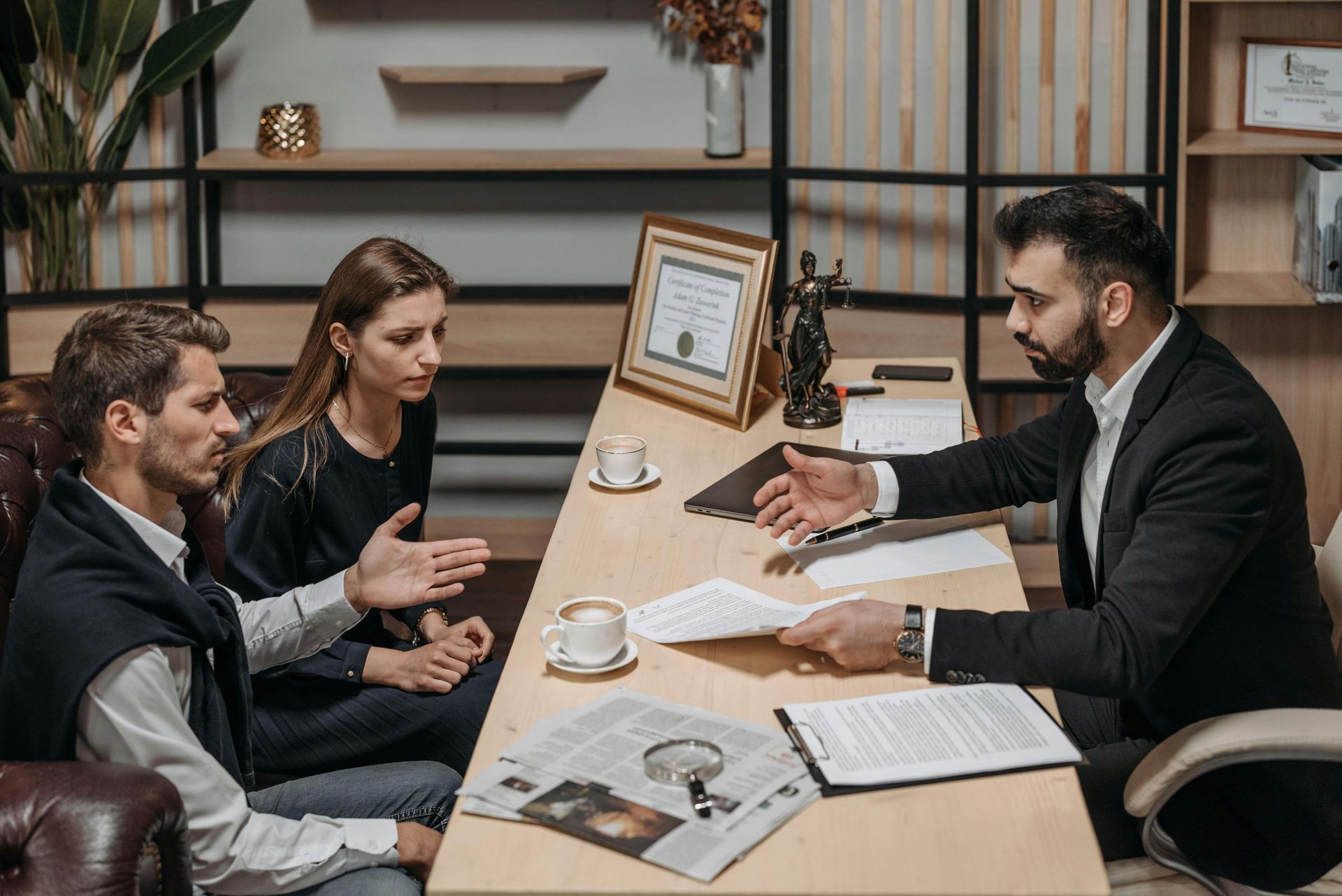 Two people in discussion with a business consultant at a desk with papers and coffee cups