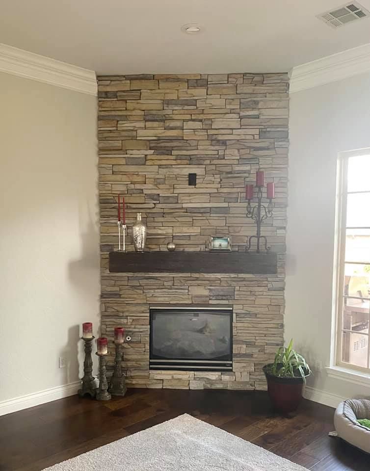 Living room with stone fireplace, mounted TV, dark wood floor, and potted plant by a bright window