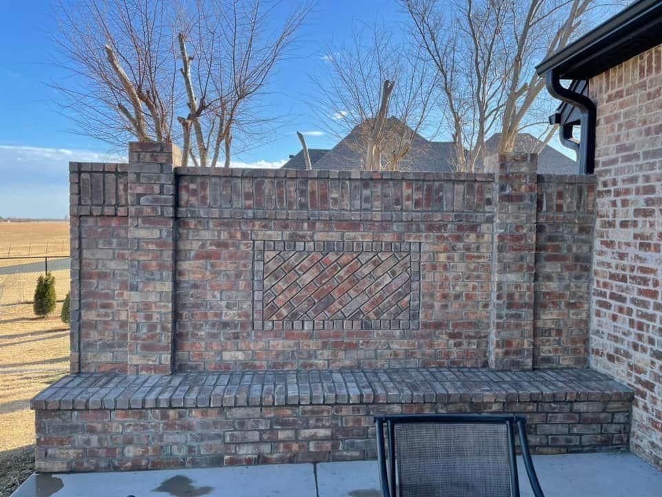Brick outdoor patio bench against a low wall with bare trees and open field beyond