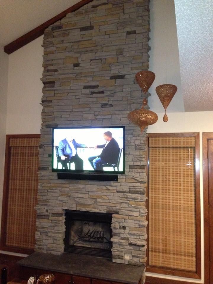 Living room fireplace with stone surround, wall-mounted TV, and decorative woven wall art