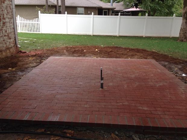 Brick patio in a backyard with a white fence and grassy yard beyond