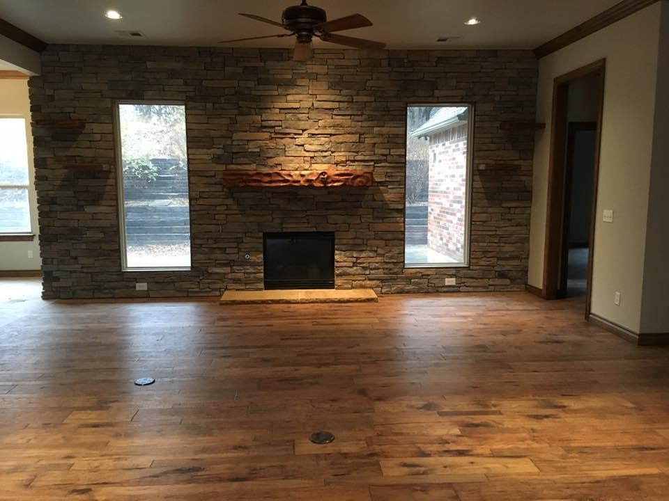 Empty living room with stone fireplace wall, wooden floor, and ceiling fan