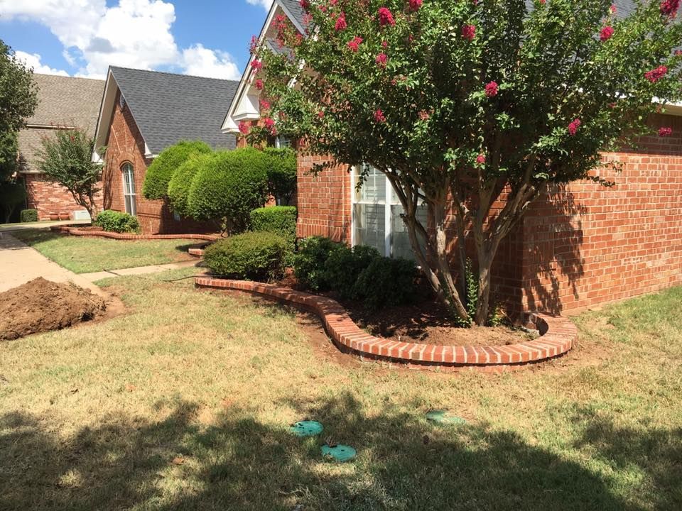 Suburban front yard with brick homes, trimmed shrubs, and a flowering tree by a brick wall