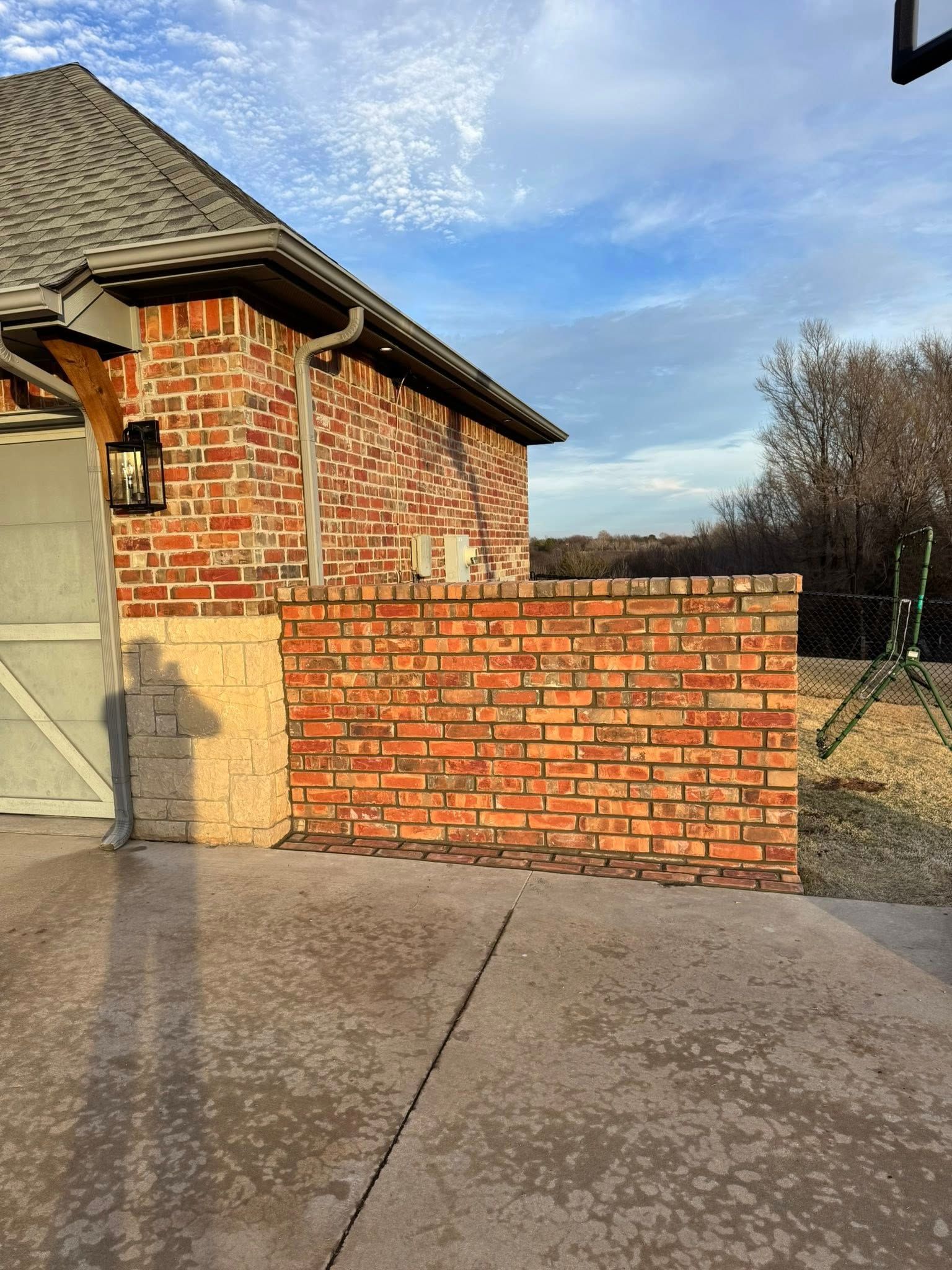 Brick wall beside a driveway next to a brick house under a blue sky