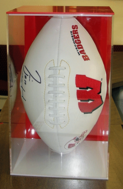 Signed white football displayed in a clear case on a red background