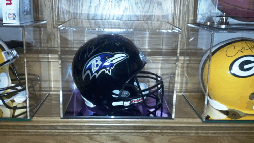 Black Baltimore Ravens football helmet displayed on a shelf beside a yellow Green Bay Packers helmet.