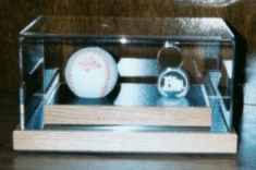 Display case with a baseball, small trophy, and folded scorecards on a wooden shelf.