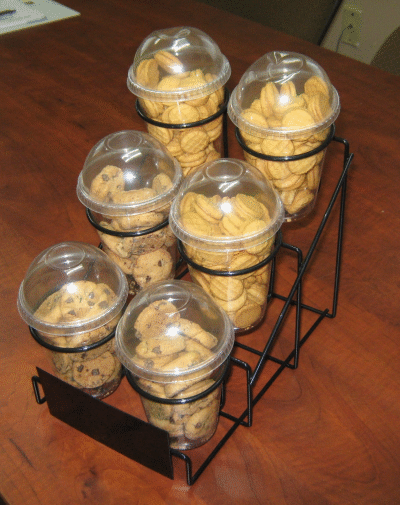 Six clear snack cups in a black wire rack on a wooden table.