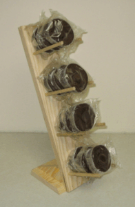 Wooden tabletop wine rack holding four bottles, angled against a plain wall.