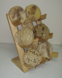 Wooden display stand holding six round, speckled baked goods or soaps arranged in two columns.